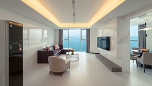 Een moderne woonkamer met een grote televisie, comfortabele zitplaatsen, een eethoek en uitzicht op zee.