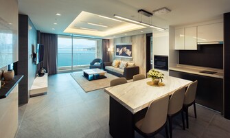 Una habitación de hotel moderna con comedor, sofá, televisión y vista al mar.