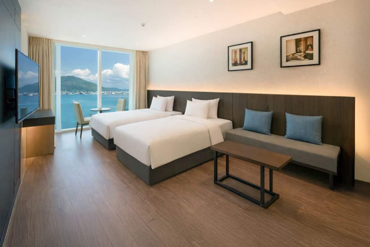 Ein Hotelzimmer mit zwei Betten, einem Sofa, einem Fernseher und einem großen Fenster mit Blick.