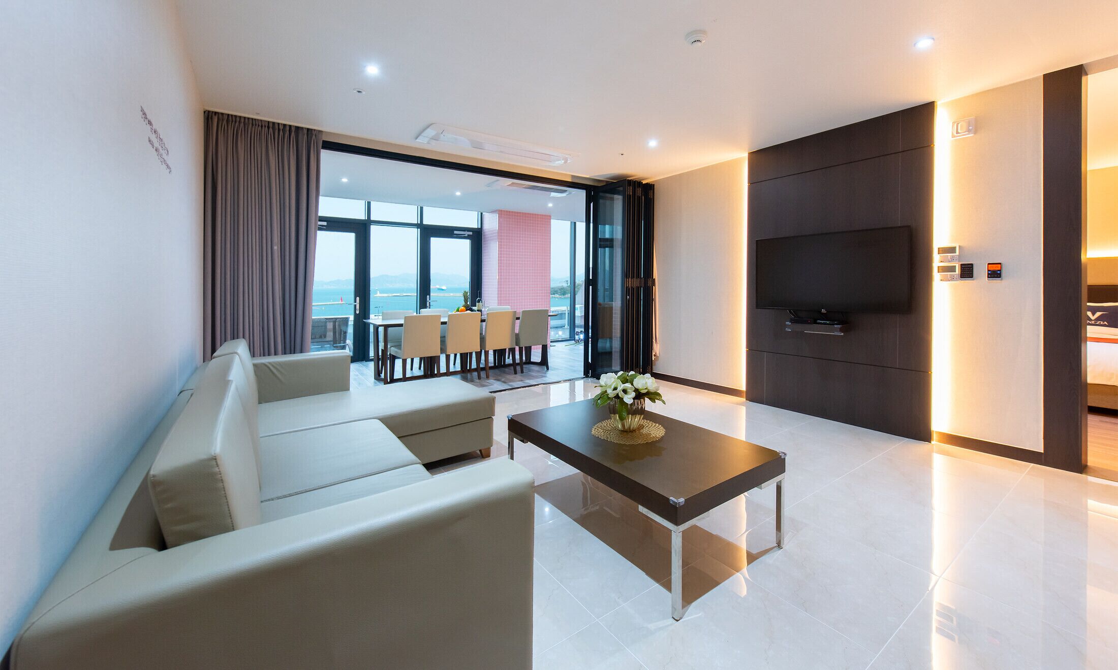 A modern living room with a sofa, a coffee table, and a TV. There is a dining area with a table and chairs.