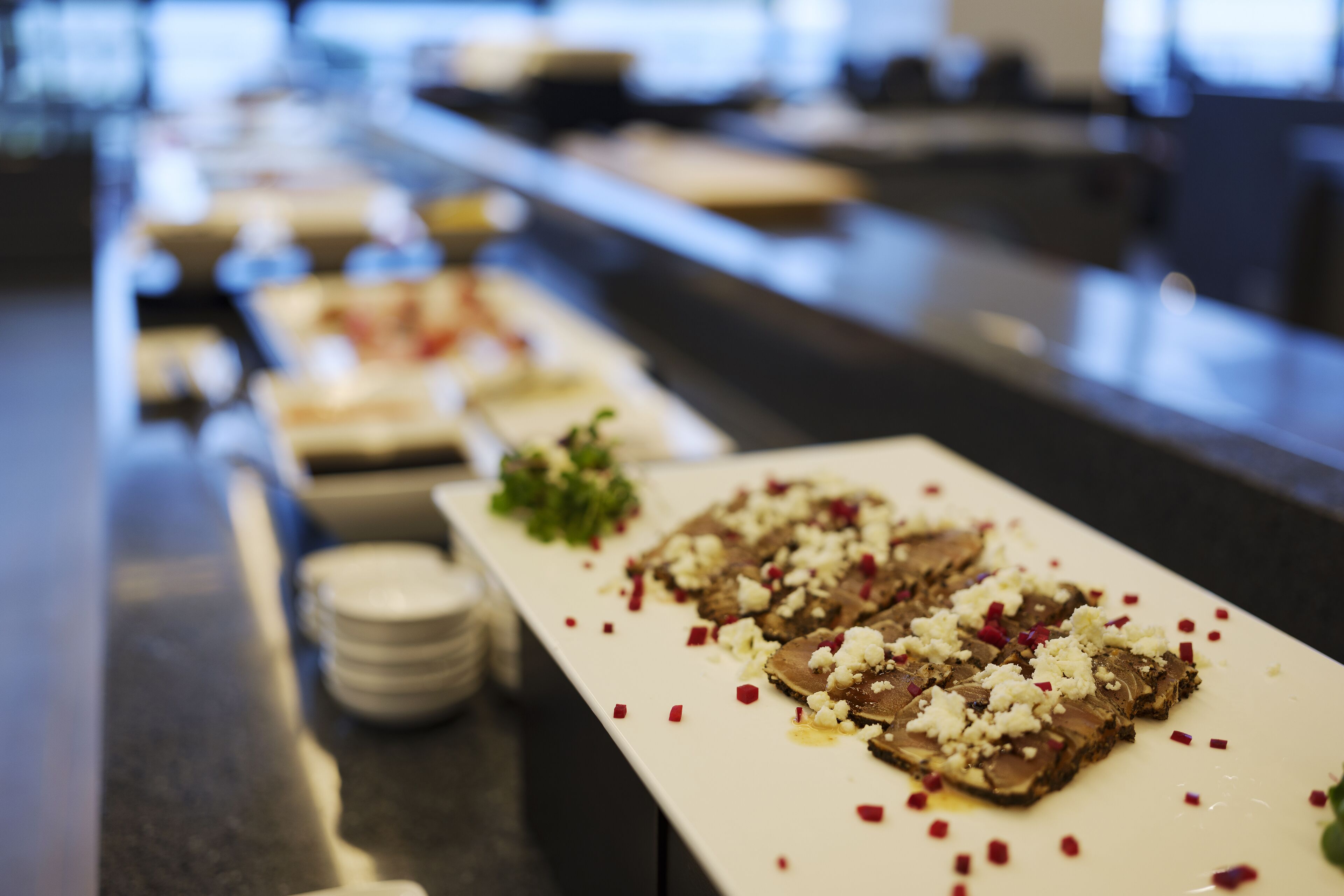 A buffet table with various dishes, including a plate with a meat dish topped with crumbled cheese and red pepper flakes.