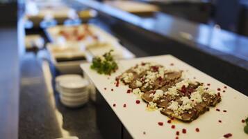 Una mesa de buffet con diversos platos, incluyendo un plato con guiso de carne coronado con queso desmenuzado y hojuelas de chile.