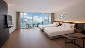 Een hotelkamer met twee bedden, een televisie, een balkon met een tafel en stoelen, en uitzicht op zee.