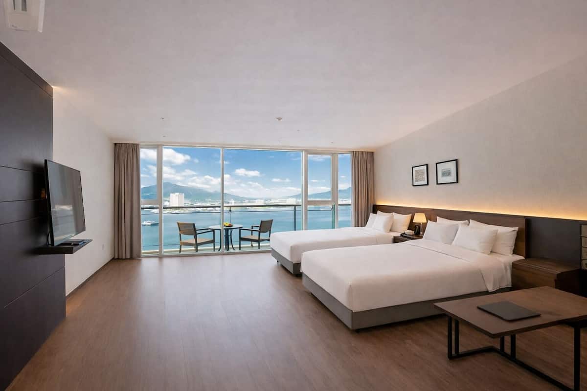 Ein Hotelzimmer mit zwei Betten, einem Fernseher, einem Balkon mit Tisch und Stühlen und Meerblick.