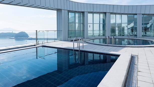 Een modern binnenzwembad met glazen balustrades en uitzicht op zee.