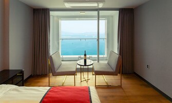 A hotel room with a bed, a small table with two chairs, and a view of the sea through large windows.