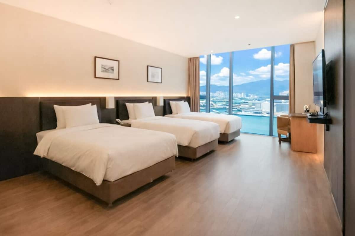 Ein Hotelzimmer mit zwei Betten, einem Fernseher und einem großen Fenster mit Blick auf die Stadt.