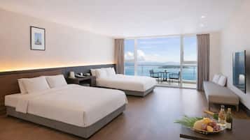 A hotel room with two beds, a balcony with a table and chairs, and a large window offering a view of the sea.