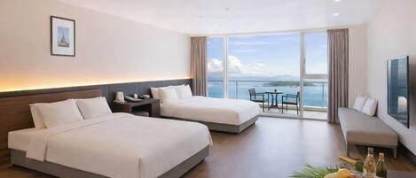 A hotel room with two beds, a balcony with a table and chairs, and a large window offering a view of the sea.