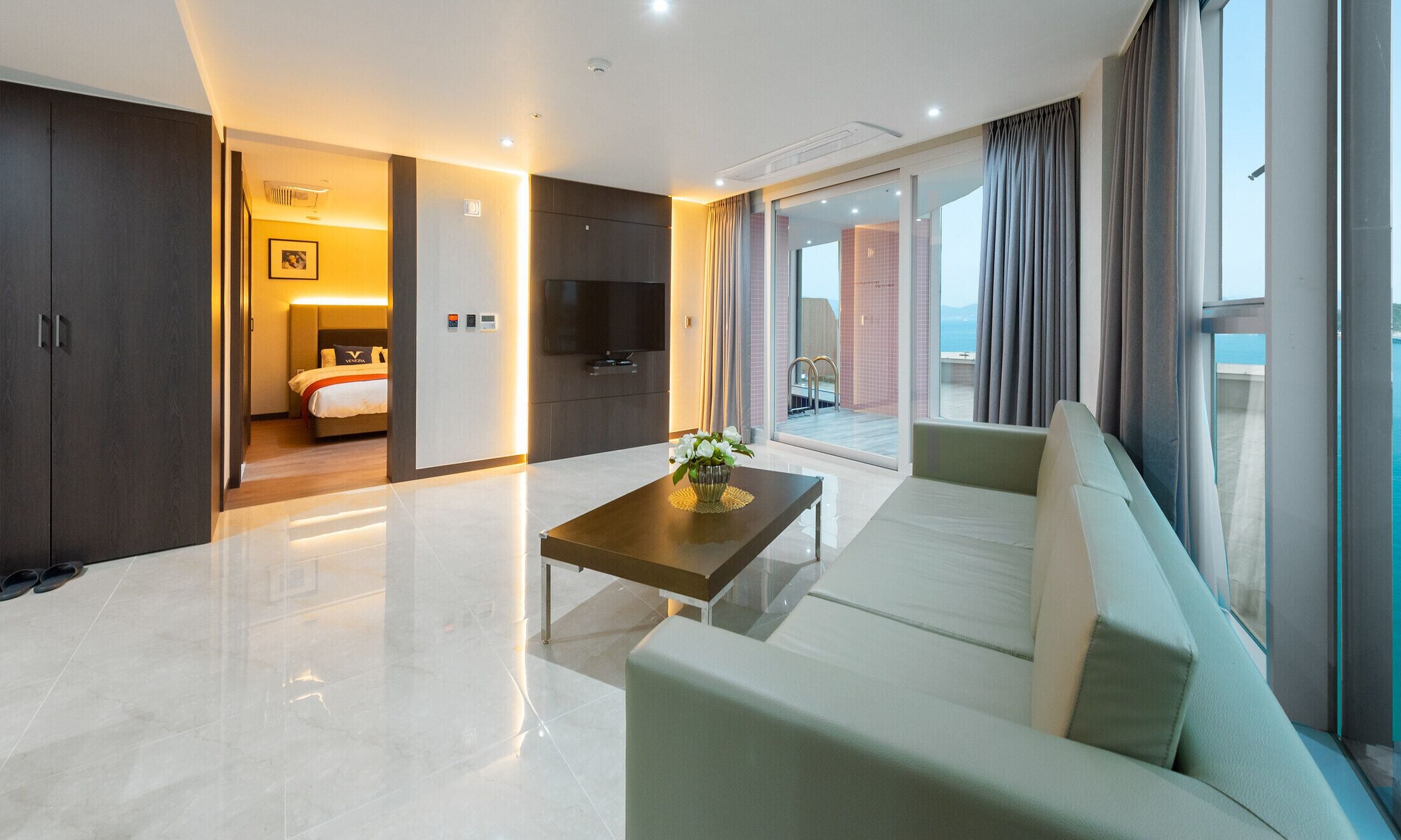 Una camera d'albergo moderna con un letto grande, una televisione, un divano e un balcone con vista.