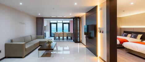 A modern hotel room with a sofa, a dining table, a TV, and a bed with a headboard.