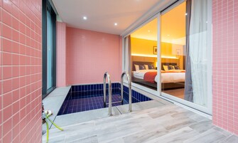 Un baño moderno con bañera, zona de ducha y puerta de vidrio que da a un dormitorio con cama y mesita de noche.