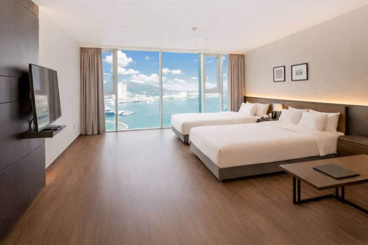 Ein Hotelzimmer mit großem Fenster, zwei Betten, einem Fernseher und einem kleinen Tisch.