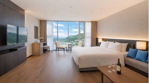A hotel room with a bed, a TV, a desk, and a view of the mountains.