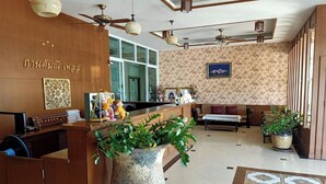 A reception area with a wooden desk, a large decorative vase, and a sofa. - Karnmanee Place Hotel (Udon Thani)