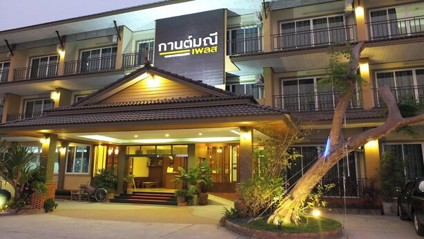 A multi-story hotel with a prominent sign, a covered entrance, and a landscaped area with a tree. - Karnmanee Place Hotel (Udon Thani)