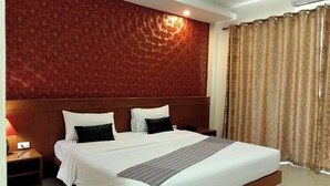 A hotel room with a large bed, a wooden headboard, a nightstand, and a wall with a decorative pattern. - Karnmanee Place Hotel (Udon Thani)