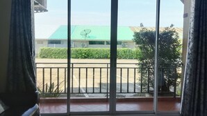 A room with a large sliding glass door leading to a balcony. The balcony has a metal railing and a view of a building with a green roof and a satellite dish. - Karnmanee Place Hotel (Udon Thani)