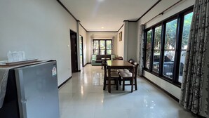 A spacious, well-lit room with a dining table and chairs, a refrigerator, and large windows offering a view of the outdoors. - Saithong Resort (Udon Thani)