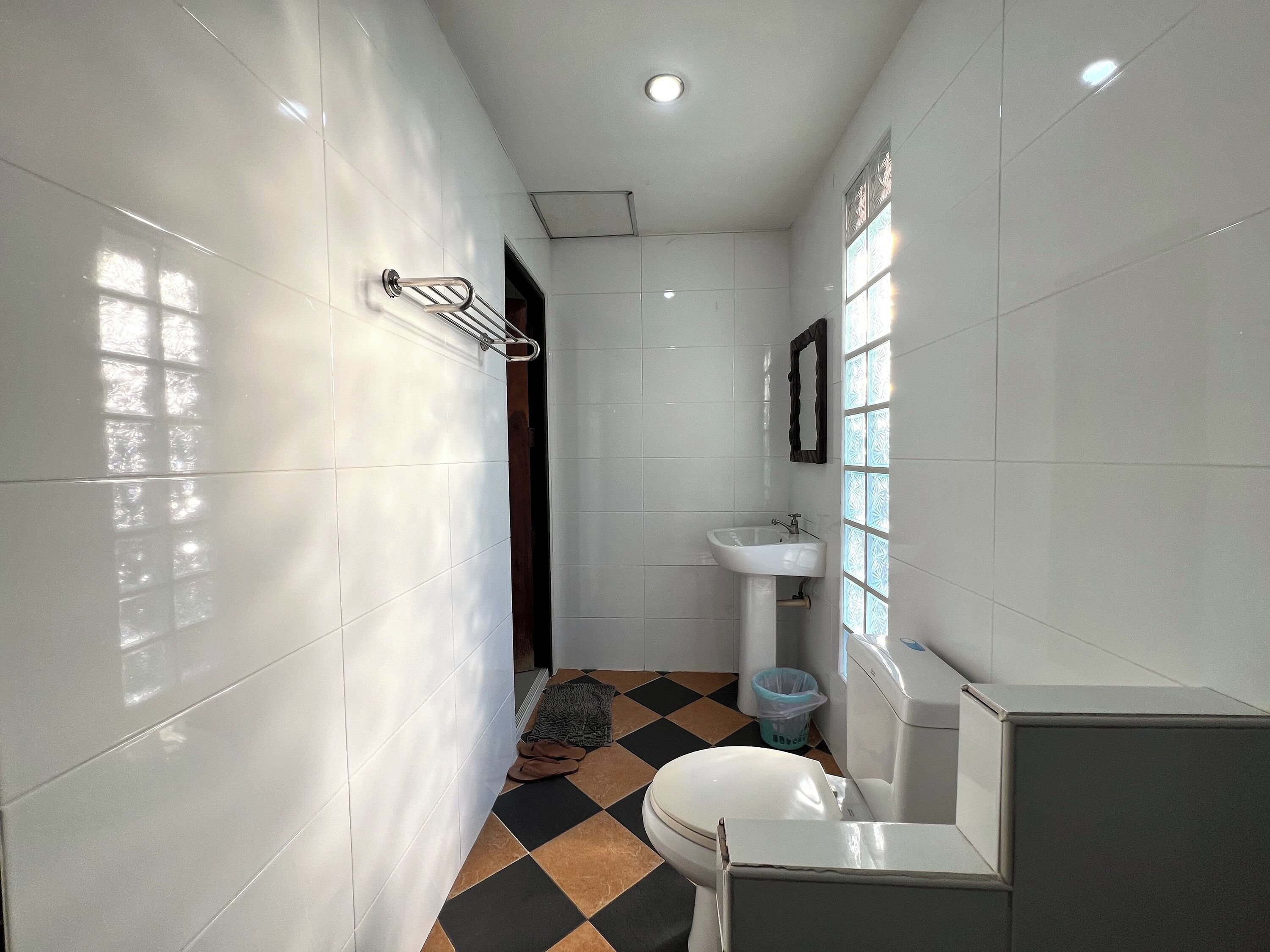 A bathroom with white tiled walls, a black and brown checkered floor, a white sink, and a toilet.