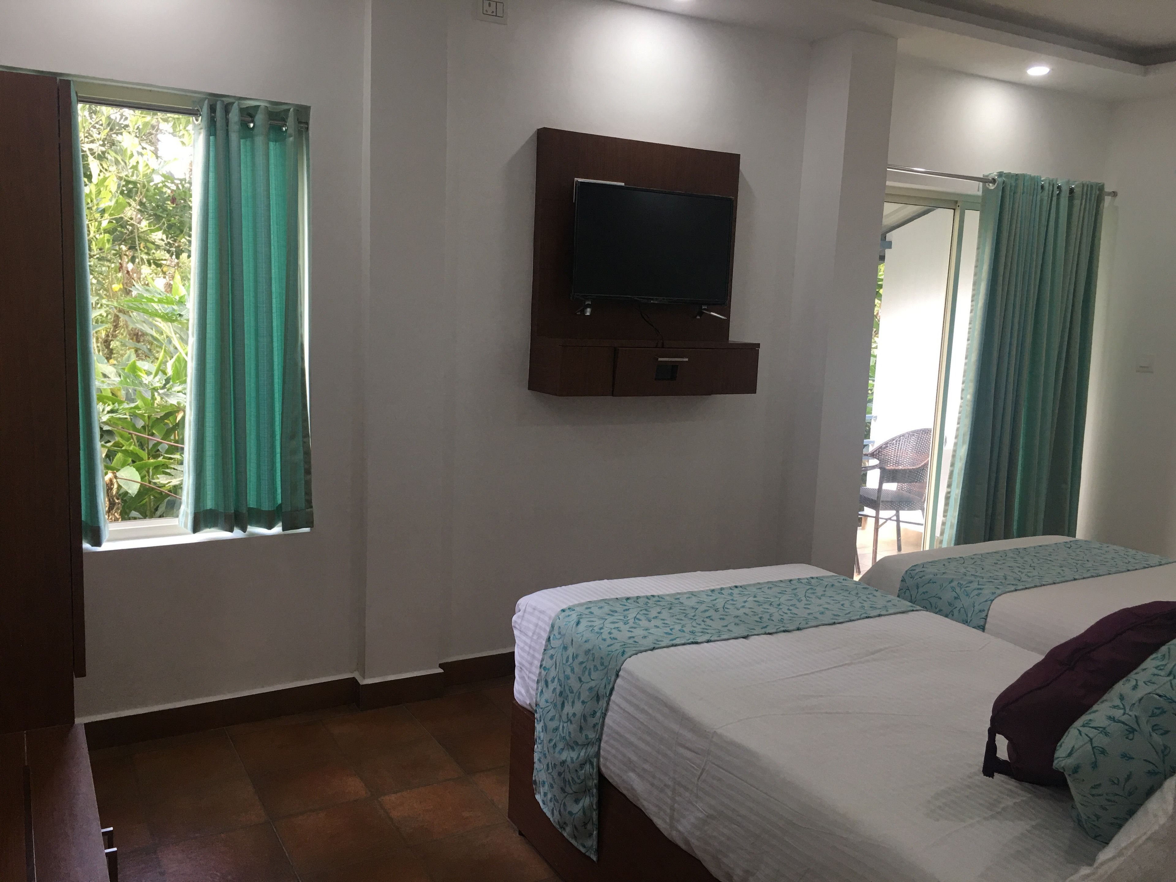 A hotel room with two beds, a TV mounted on the wall, and a window with curtains.