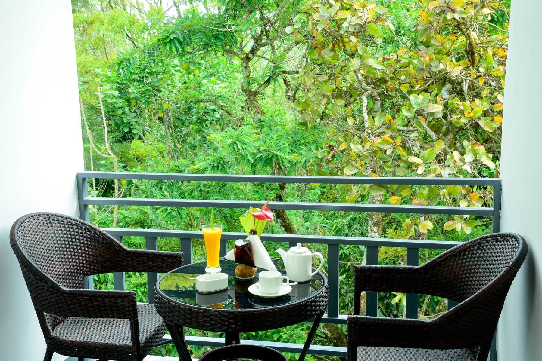 Een balkon met rieten stoelen en een ontbijttafel.