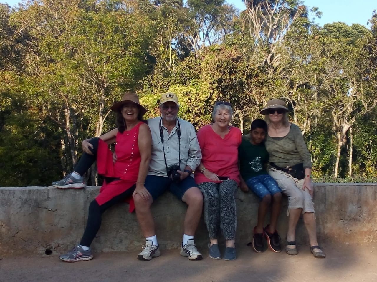 A group of people sitting on a concrete ledge with trees in the background.