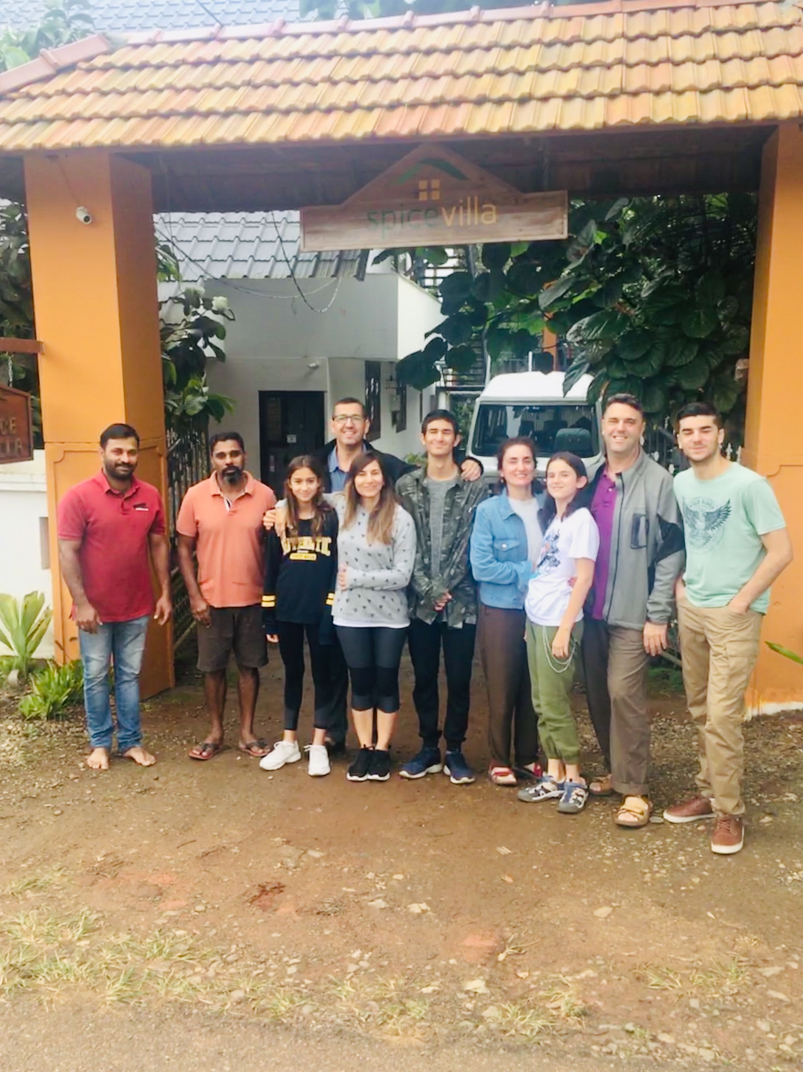 A group of people standing in front of a building with a tiled roof and a sign that reads "spicevilla".