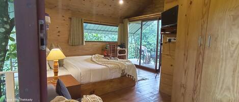 Un dormitorio de cabaña de madera con una cama, una lámpara, un televisor y un ventanal corredera que da a un balcón.