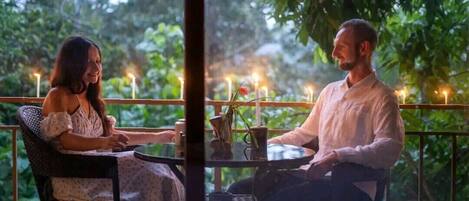 Dos personas sentadas en una mesa al aire libre con velas, rodeadas de vegetación.