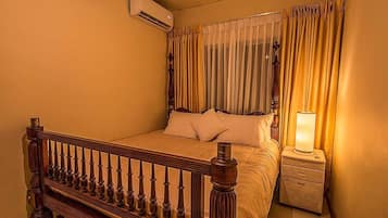 A bedroom with a wooden bed, a nightstand with a lamp, and a window with curtains.