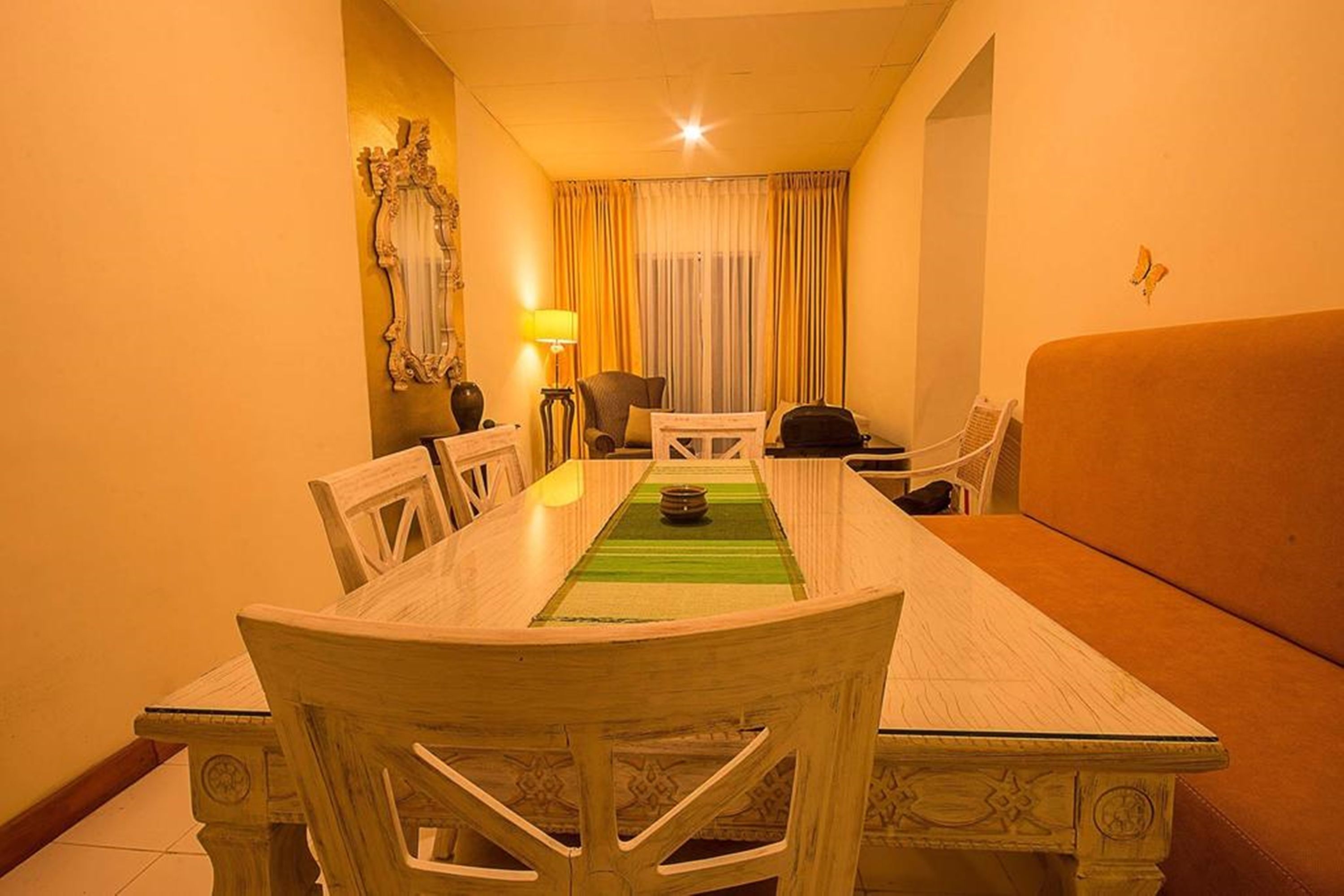 A hotel room with a dining table, chairs, a sofa, a lamp, and a decorative mirror.