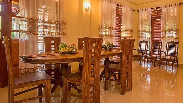 A dining area with a long wooden table, several chairs, and a fruit bowl. - Arathi Appartment (Galle)