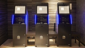 Tres cajeros automáticos con luces azules iluminadas, frente a una pared de madera.