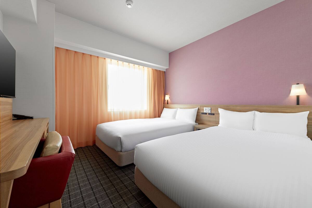 A hotel room with two beds, a desk with a chair, a TV, and a window with curtains.