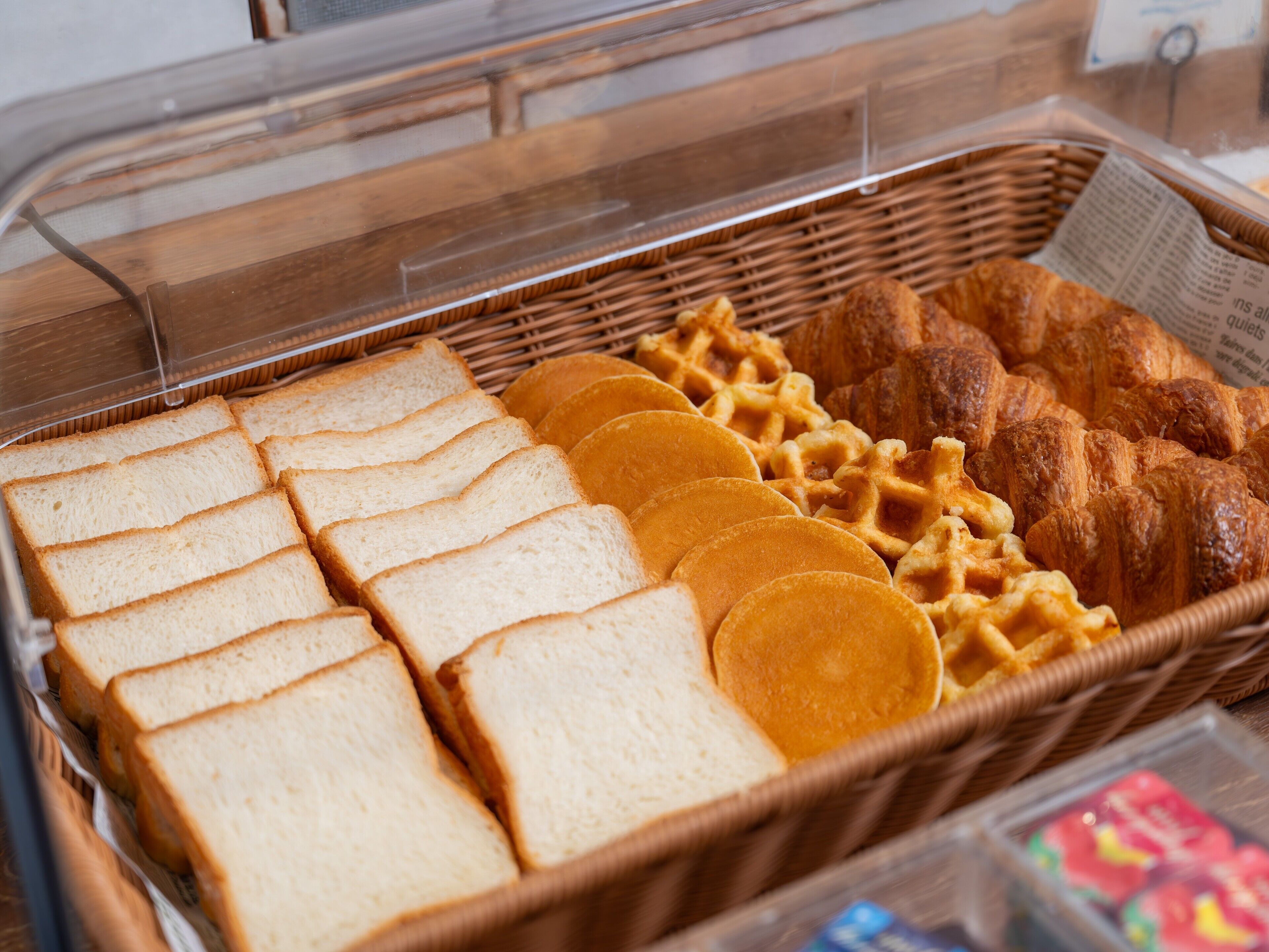 A bakery display with sliced bread, waffles, and croissants.