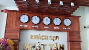 A reception area with a wooden panel wall, clocks displaying time in various cities, and a sign with Vietnamese text. - Nhat Tan Hotel (Quy Nhon)