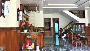 A hotel lobby with a wooden reception desk, a staircase, and a chandelier. - Nhat Tan Hotel (Quy Nhon)