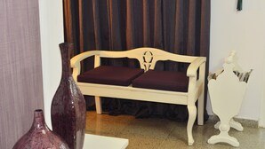 Ein Zimmer mit einem weißen Sofa, zwei dunklen Kissen, einem weißen Tisch und einer weißen Dekotruhe mit Zeitschriften.