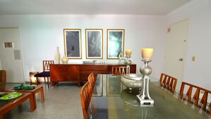 Ein Essbereich mit einem Glastisch, Holzsesseln, einem Holzschrank und gerahmten Bildern an der Wand.