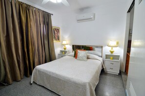 Una camera d'albergo con un letto, due comodini con lampade, un condizionatore d'aria e una tenda.