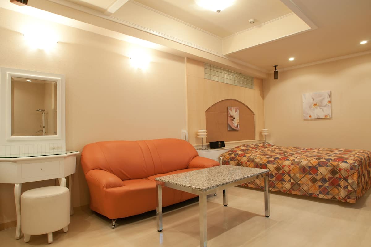 Un dormitorio con cama, sofá, mesita, mesita de noche y espejo.