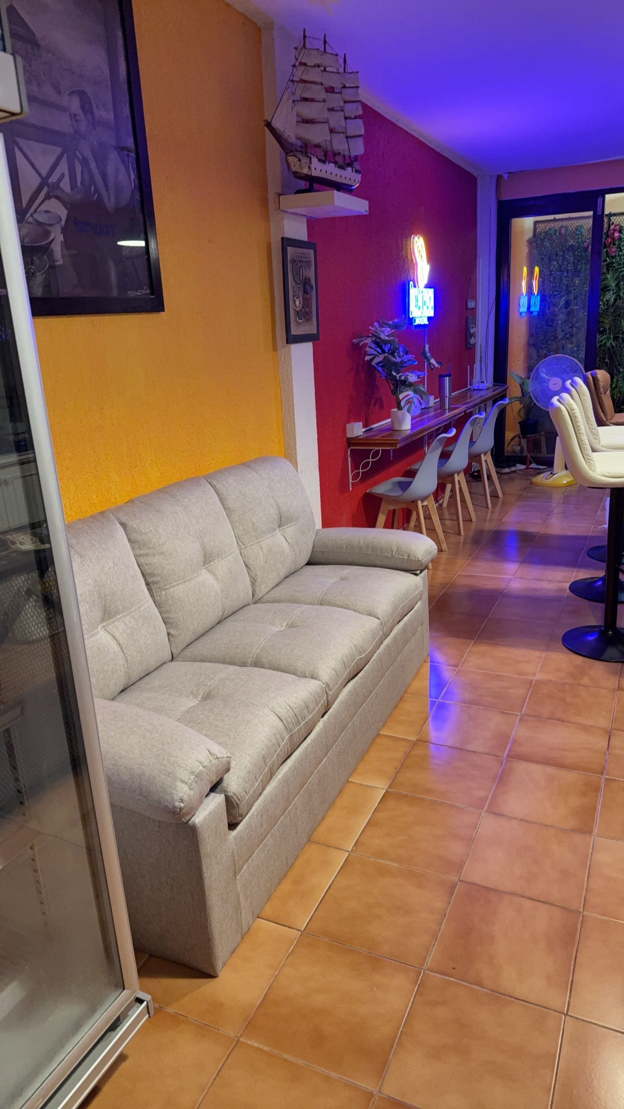A living room with a grey sofa, a small table with a plant, and a neon sign.