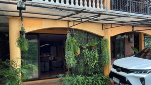 Ein Haus mit Balkon, ein weißes Auto davor und verschiedene Kübelpflanzen.