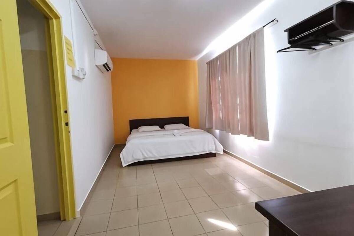 Un dormitorio con cama, ventana con cortinas, unidad de aire acondicionado y puerta.