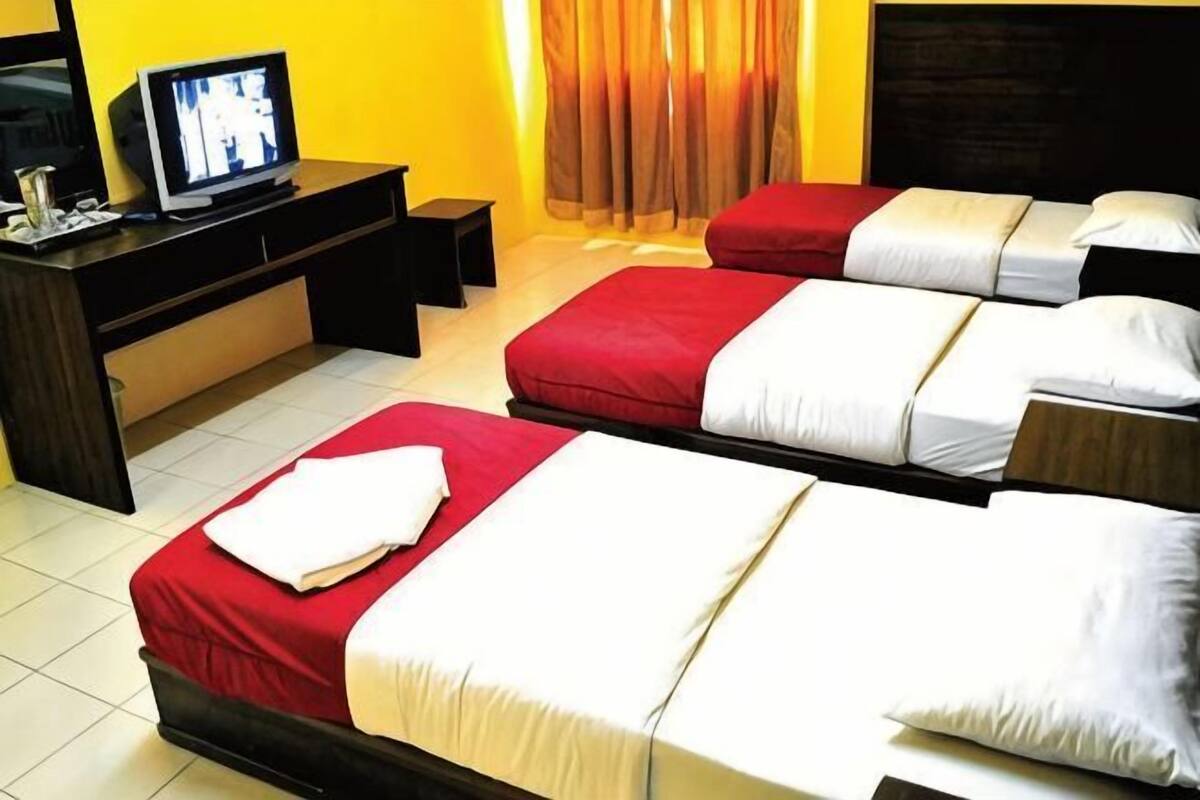 Una habitación de hotel con tres camas, televisión y escritorio.