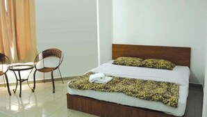 Una habitación de hotel con cama, dos sillas, una mesita y ventana con cortinas.