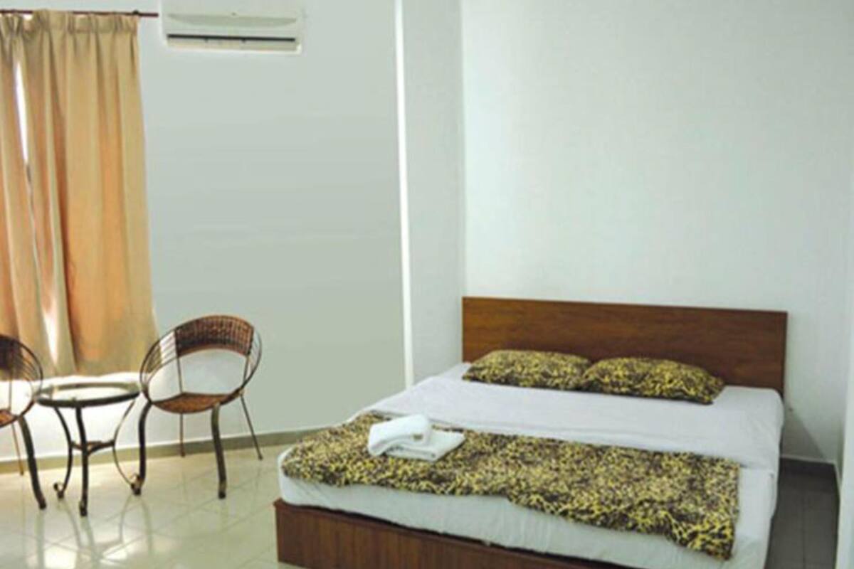 Una habitación de hotel con cama, dos sillas, una mesita y ventana con cortinas.