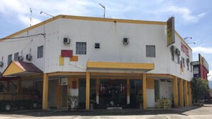 Un hotel de dos pisos con fachada amarilla y blanca, múltiples unidades de aire acondicionado y un letrero que indica que es un hotel.