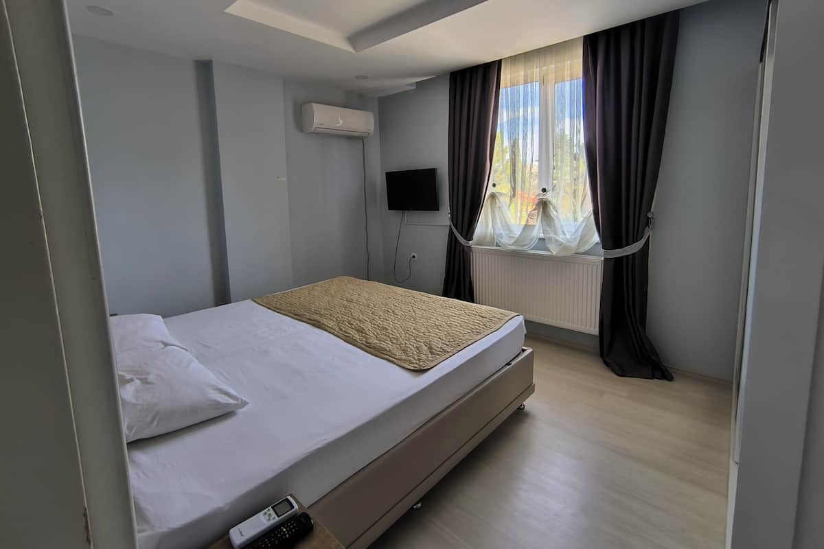 Moderni hotellihuone, jossa on yksi sänky, seinälle asennettu taulutelevisio ja ikkuna, jossa on verhot.
